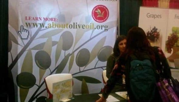 A booth for the North American Olive Oil Association with a banner and a person interacting with staff. - Olive Oil Times