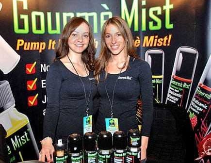 Two women posing with Gourmè Mist products at a promotional event. - Olive Oil Times