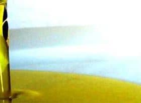 Olive oil being poured from a container into a pool of oil on a surface. - Olive Oil Times
