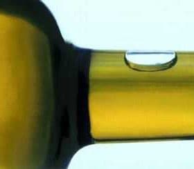 Close-up view of the neck of an olive oil bottle with a droplet of oil on the surface. - Olive Oil Times