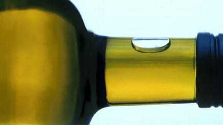 Close-up view of the neck of an olive oil bottle with a droplet of oil on the surface. - Olive Oil Times