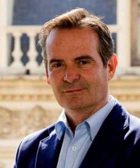 Man wearing a blue blazer and light blue shirt, standing with a neutral expression. - Olive Oil Times