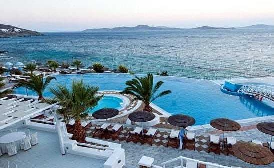 Infinity pool with palm trees and lounge chairs beside the sea at a resort. - Olive Oil Times