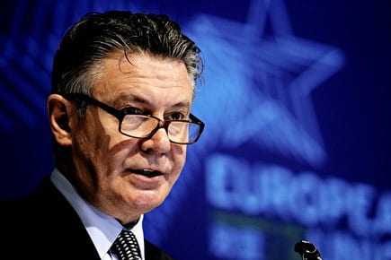 Karel De Gucht delivering a speech at a podium during a conference with a blue background. - Olive Oil Times