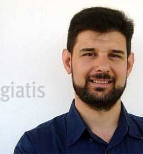 Man with a beard wearing a blue shirt, smiling against a plain background with the name 'Magiatis' next to him. - Olive Oil Times