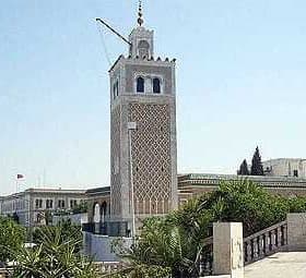 Clock tower with intricate design and a spire located in Tunisia, surrounded by greenery. - Olive Oil Times