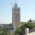 Clock tower with intricate design and a spire located in Tunisia, surrounded by greenery. - Olive Oil Times