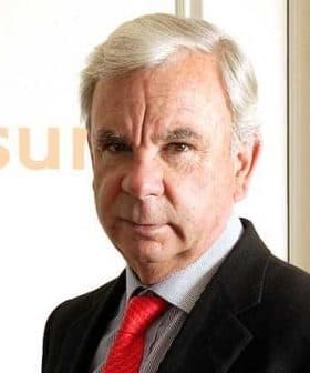 Man in a black suit and red tie posing for a portrait against a light background. - Olive Oil Times