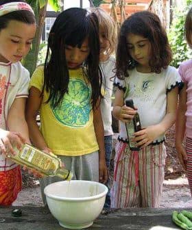 Group of children pouring olive oil into a bowl while cooking together outdoors. - Olive Oil Times