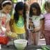Group of children pouring olive oil into a bowl while cooking together outdoors. - Olive Oil Times