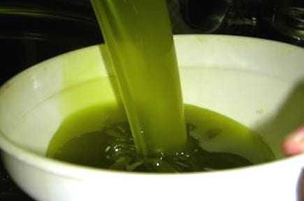Green olive oil being poured from a container into a white bowl. - Olive Oil Times