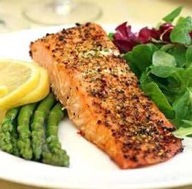 Grilled salmon fillet served with asparagus, lemon slices, and mixed salad greens on a white plate. - Olive Oil Times