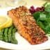 Grilled salmon fillet served with asparagus, lemon slices, and mixed salad greens on a white plate. - Olive Oil Times