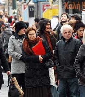 Group of people waiting at a bus stop, some wearing winter clothing and holding items. - Olive Oil Times