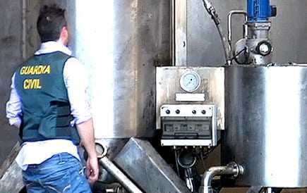 Civil Guard officer in a blue vest examining industrial equipment in a facility. - Olive Oil Times