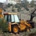 Yellow backhoe loader working in an olive grove, with an olive tree in the background. - Olive Oil Times