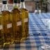 Four bottles of olive oil arranged on a checkered tablecloth with glasses nearby. - Olive Oil Times