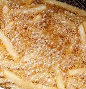 Fried potato strips bubbling in hot oil during the cooking process. - Olive Oil Times
