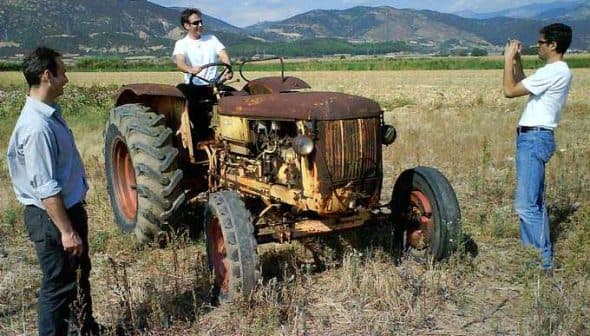 A vintage tractor in a field with two men standing nearby, one taking a photo. - Olive Oil Times