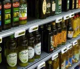 Multiple bottles of olive oil displayed on shelves in a grocery store. - Olive Oil Times