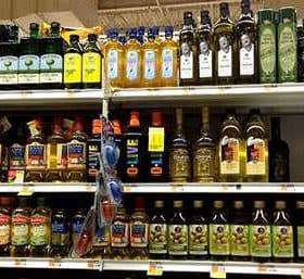Multiple bottles of olive oil displayed on a grocery store shelf in various sizes and brands. - Olive Oil Times