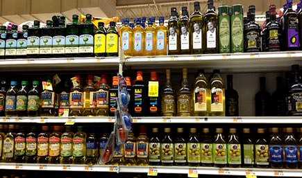 Multiple bottles of olive oil displayed on a grocery store shelf in various sizes and brands. - Olive Oil Times