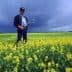 A man holding a flower while standing in a field of yellow flowers under a cloudy sky. - Olive Oil Times