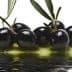 A cluster of black olives resting in olive oil with a reflective surface. - Olive Oil Times
