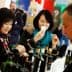 Two women sampling olive oil at a trade show, one holding a tasting cup and the other observing. - Olive Oil Times