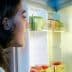 A person with dark hair looking into an open refrigerator filled with various food items and a bottle of oil. - Olive Oil Times