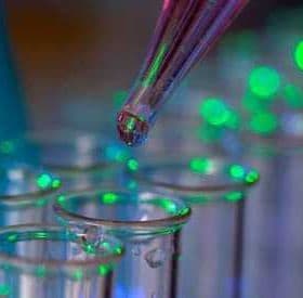 A pipette dropping liquid into a row of clear test tubes illuminated with green light. - Olive Oil Times