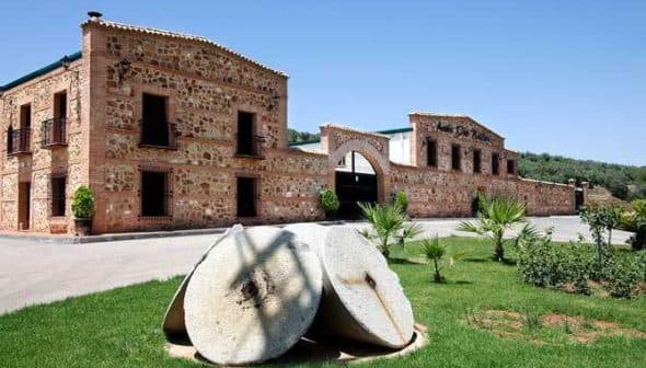 Exterior view of an olive oil mill featuring large stone grinding wheels in the foreground. - Olive Oil Times