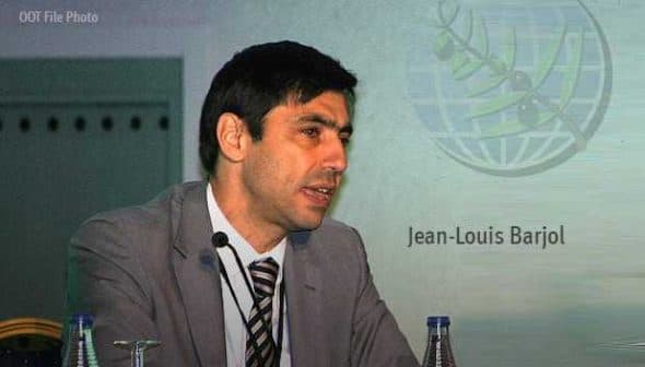 Jean-Louis Barjol speaking at a conference with a logo in the background. - Olive Oil Times
