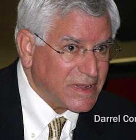 Darrel Corti engaged in conversation during a public event, wearing glasses and a suit. - Olive Oil Times