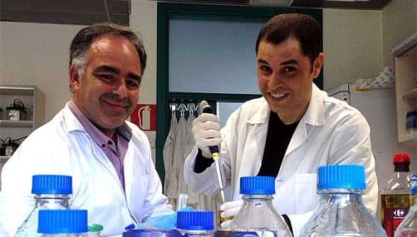 Two male scientists wearing lab coats and gloves working with laboratory equipment and bottles. - Olive Oil Times