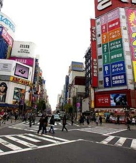 A busy intersection in Tokyo featuring large advertisements and pedestrians crossing the street. - Olive Oil Times