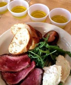 A plate featuring sliced roast beef, bread, and small cups of olive oil arranged on a table. - Olive Oil Times