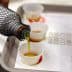 A bottle pouring olive oil into small tasting cups on a tray. - Olive Oil Times