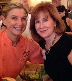Two women smiling and posing for a photo at a social event, one wearing an orange chef's jacket. - Olive Oil Times