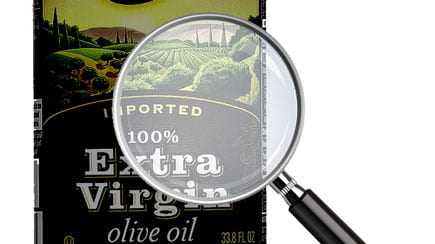 Bottle of extra virgin olive oil with a magnifying glass focusing on the label details. - Olive Oil Times