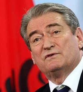 Man speaking at a podium with an Albanian flag in the background. - Olive Oil Times