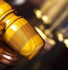 Close-up of a wooden gavel with scales of justice blurred in the background. - Olive Oil Times