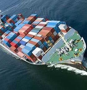 Aerial view of a cargo ship loaded with colorful shipping containers on water. - Olive Oil Times