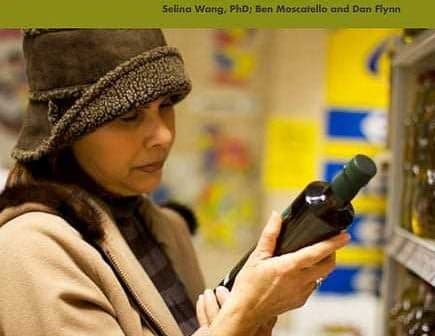 Woman examining a bottle of olive oil while holding a survey document titled 'Consumer Attitudes on Olive Oil'. - Olive Oil Times