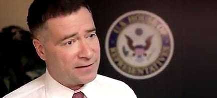 Man in a white shirt and tie speaking in front of a U.S. government seal. - Olive Oil Times