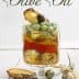 Book cover for 'Cooking Techniques with Olive Oil' featuring a glass container with layered ingredients and herbs. - Olive Oil Times