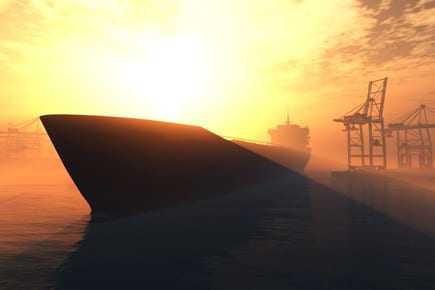 Silhouette of a large ship against a sunset backdrop with cranes in the background. - Olive Oil Times
