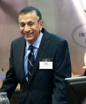 A man in a dark suit and tie standing at a podium during a conference presentation. - Olive Oil Times