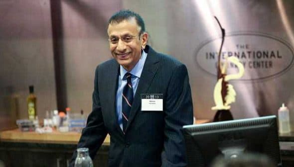 A man in a dark suit and tie standing at a podium during a conference presentation. - Olive Oil Times