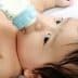 Infant with dark hair drinking from a blue baby bottle while lying down. - Olive Oil Times